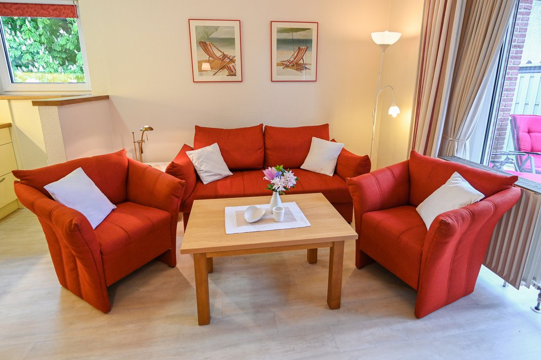 Wohnzimmer der Ferienwohnung 15 mit roter Polstergarnitur, breiten Wegen und Terrassentür